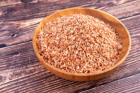 Raw brown whole rice in a bowl over wooden table.の写真素材