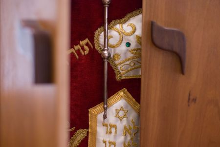The doors of a wooden ark are beginning to open and reveal the holy Torah draped in a red dress and adorned with silver and gold decorations inside.の写真素材
