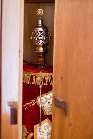 The doors of a wooden ark are beginning to open and reveal the holy Torah draped in a red dress and adorned with silver and gold decorations inside.の写真素材