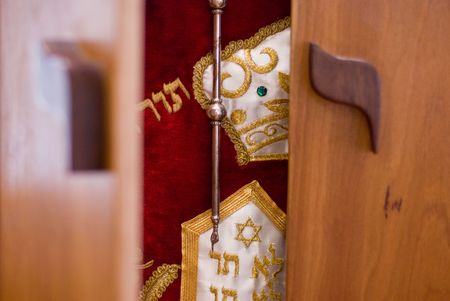 The doors of a wooden ark are beginning to open and reveal the holy Torah draped in a red dress and adorned with silver and gold decorations inside.の写真素材