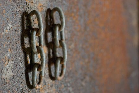 Solid steel chain links hang against the rusting interior walls of a boat awaiting restoration.の写真素材