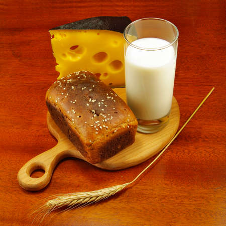 image of a glass of milk, bread on the board, wheat and cheese closeupの写真素材