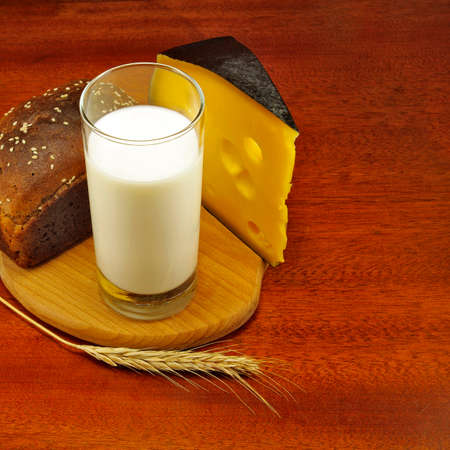 image of a glass of milk, bread on the board, wheat and cheese closeupの写真素材