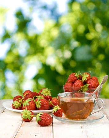 image of strawberries on a plate and cup of tea on green backgroundの写真素材