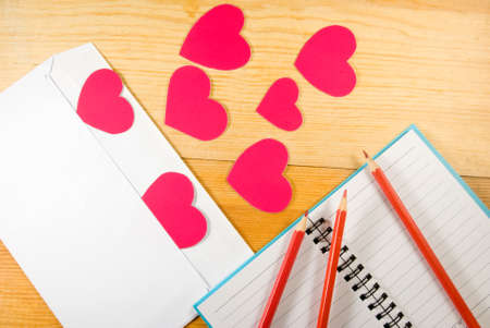 image of envelopes, notebooks, pencils, and paper hearts on a wooden table close-upの写真素材