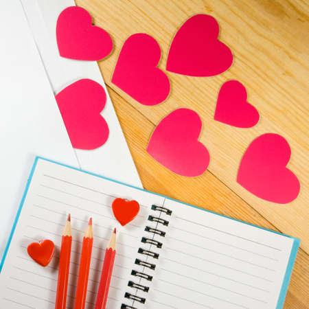 image of envelopes, notebooks, pencils, and paper hearts on a wooden table closeup