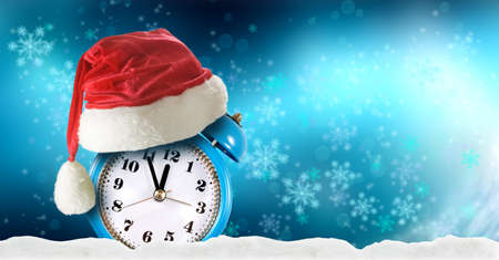 image of alarm clock and red christmas hat on winter abstract blue background