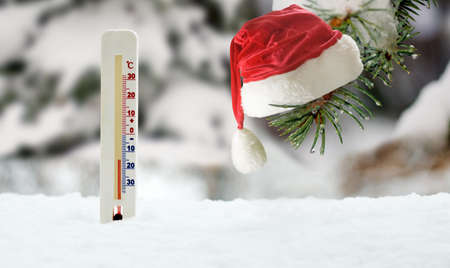 An image of a thermometer inserted into the snow and a Christmas hat hanging on a fir branch