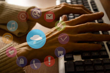 Female hands on laptop keyboard and image overlay of weather icon and other various internet icons