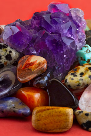 Image of semi-precious stones lie in a heap and on top of a heap a beautiful amethyst on a red background close-upの写真素材