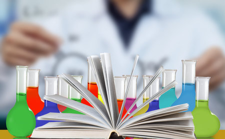 Image of open book, behind which there are flasks filled with liquid against the background of a blurred figure of a man in a white coatの写真素材