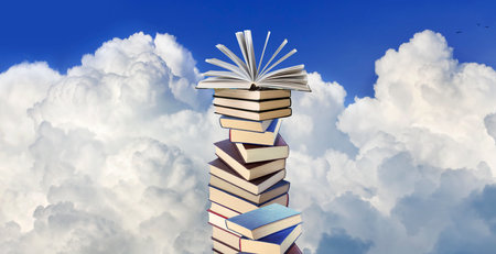 Image of a stack of books with an open book lying on top of the stack against a background of white cloudsの写真素材