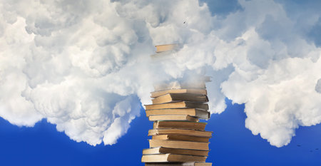 A tall stack of books reaches up through the fluffy white clouds on a bright, blue day.