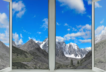 A scenic view of snow-capped mountains through a double-paned window on a bright, sunny afternoon.