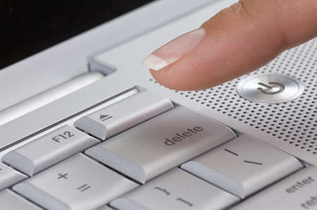 Close-up of manicured female finger about to press the delete buton on a silver laptop keyboardの写真素材