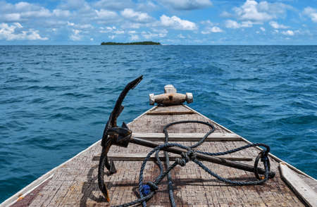 Old wooden boat bow with rusty anchor approaching tropical island in the Indian Oceanの写真素材
