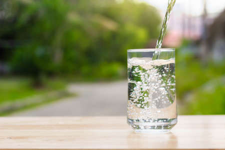 water glass on wooden table outdoors and green background.の写真素材