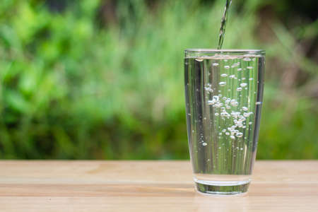 water glass on wooden table outdoors and green background.の写真素材