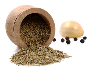 Dried rosemary leaves scattered from a wooden bowl with garlic and peppercorns isolated on a white backgroundの写真素材