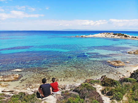 Happy couple contemplating the turquoise blue sea in a heavenly landscapeの写真素材