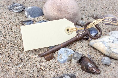 Old Key with pendant, stones and shells in beach sandの写真素材