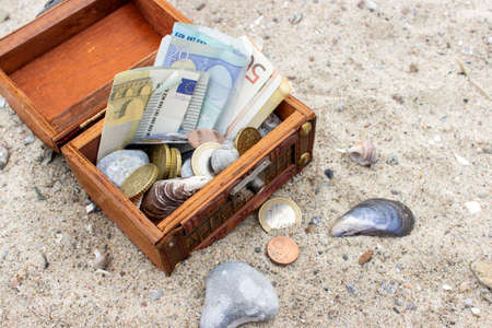 Wooden box with euro notes and coins in the sandの写真素材