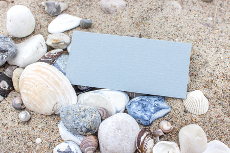 blue card with sea shells and stones on the sandy beachの写真素材