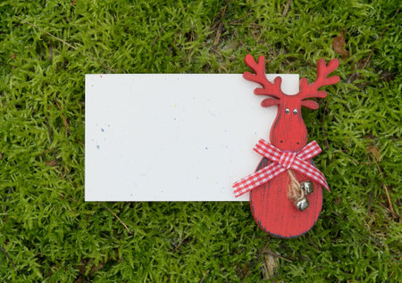 Greeting card with red reindeer figure on green moss surface and copy spaceの写真素材