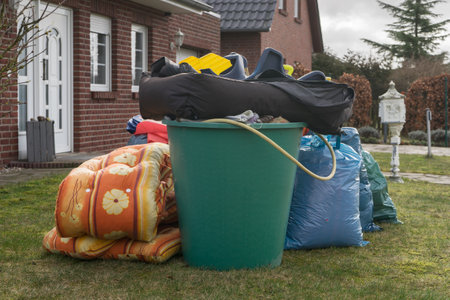 Pile of bulky waste in front of a house with garbage bags and rain barrelsの写真素材