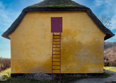 Old yellow house with a red ladder and a blue sky in the backgroundの写真素材