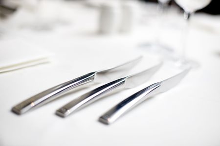 knives lined up on a white table cloth in a restaurantの写真素材