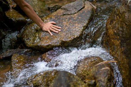 Rock, waterfall, natural source, hands touch, wet rock, water flowing through the concept, close to nature and preserve natural water sources, forests in Thailand.の写真素材