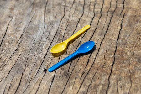 bright colored plastic spoons on wooden table blue and yellow spoonの写真素材