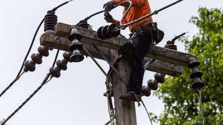 Rural electric poles are being repaired by electricians installing wires to connect. The tops of the electric poles are attached to the insulator. It is a job at a high rate.の写真素材