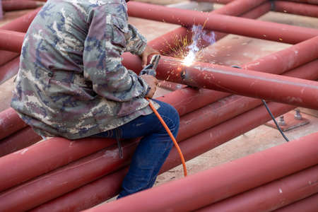 A large red iron pole Being welded by a welder On the construction site The iron was painted with red rust-proof paint.の写真素材