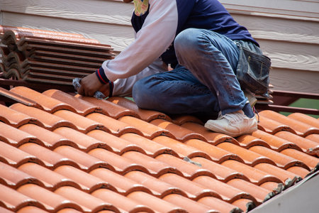 New orange roof tiles, thick plan, are being assembled on the roof by the builders. It is a very dangerous job. By skilled technicians working in Thailand building construction workの写真素材