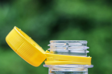 A plastic bottle cap with tamper evident ring open on transparent bottle neck, isolated on green blurred background, close up detail of packaging container