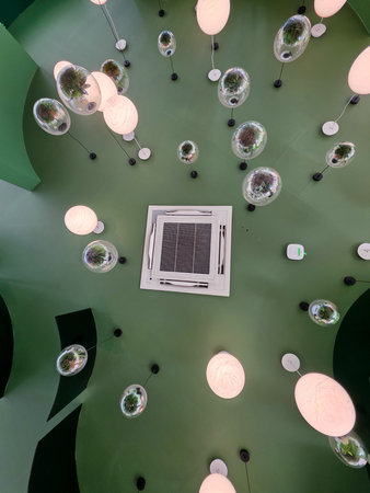 Looking upward at calm modern green ceiling featuring round glass pendant light design. contemporary interior space creates peaceful atmosphere with glowing illuminated architectural detail
