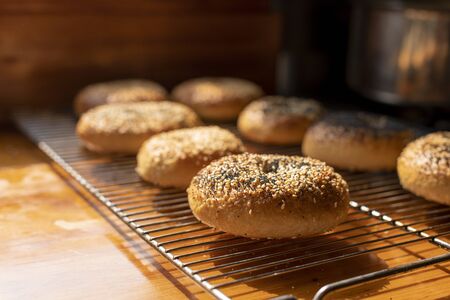 Freshly baked bagels resting on a wire tray on a wooden kitchen bench
