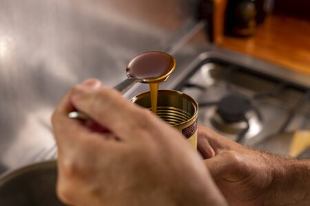 View of chef's hand measuring syrup with a spoon over a stove