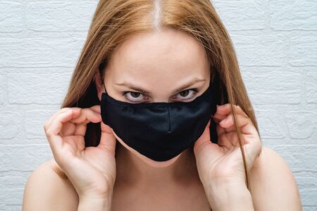 Beautiful girl puts on a black medical mask against a brick wall. danger of the virus. the epidemic is near.の写真素材