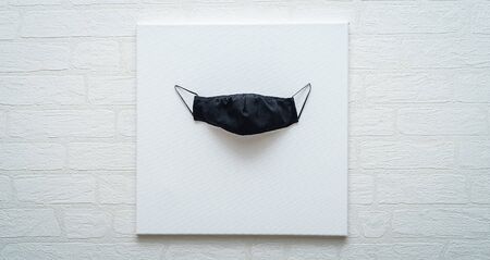 Black medical mask hanging on a canvas against a white wallの写真素材