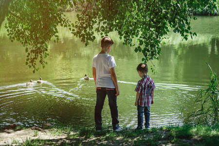 Two young boys playing fishing with sticks near pond in fall park. Little brothers having fun near lake or river in autumn.の写真素材