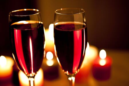 two glasses of red wine with candles in the backgroundの写真素材