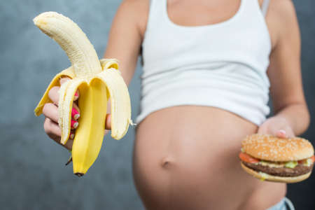 Close up of a cute pregnant belly tummy and healthy not healthy food. Pregnant female healthy...