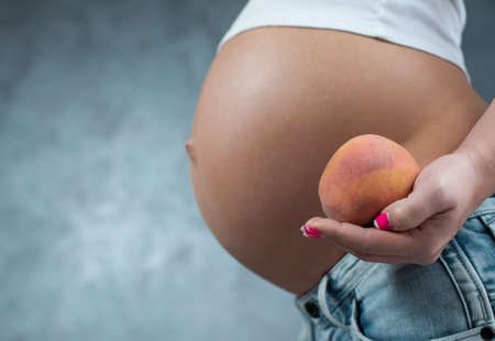 Close up of a cute pregnant belly and healthy food. Pregnant female healthy motherhood concept. Side...
