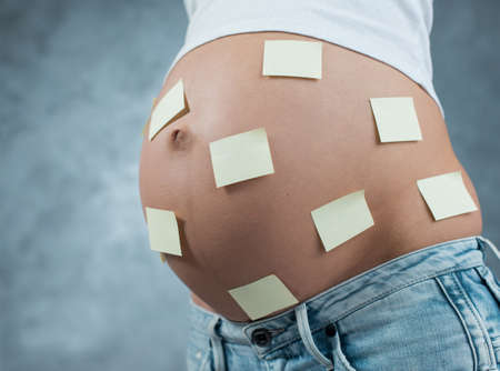 Close up of a cute pregnant belly and stickers on it. Pregnant female motherhood concept. Side view,...