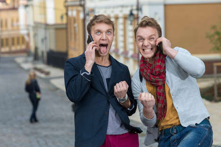 Cheerful day of twin brothers. Two stylish and handsome adult twin brothers are talking on cell...