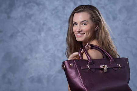 Positive emotional portrait of young and pretty girl. Portrait of beautiful woman holding a stylish clatch. Bags accessories advertising conceptの写真素材