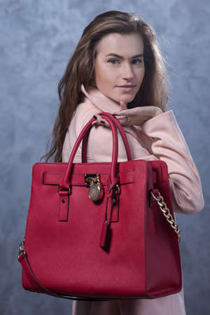 Positive emotional portrait of young and pretty girl. Portrait of beautiful woman holding a stylish clatch. Bags accessories advertising conceptの写真素材